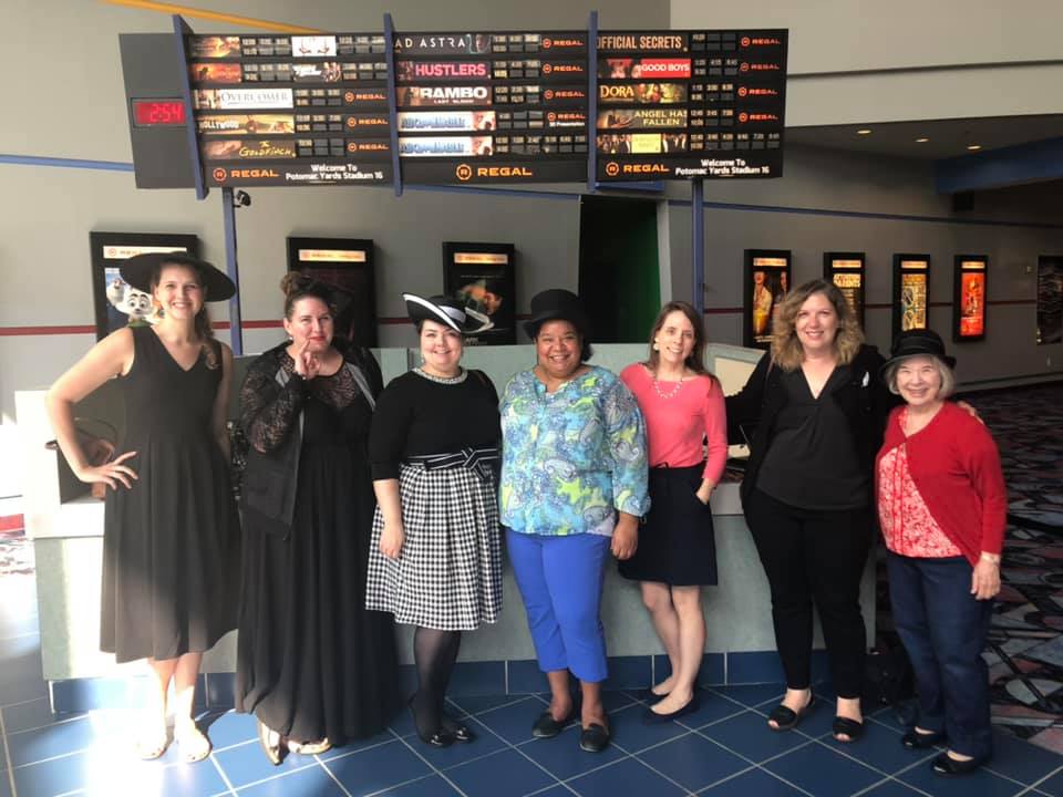 Group photo of women, several in formal hats, in lobby of movie theater