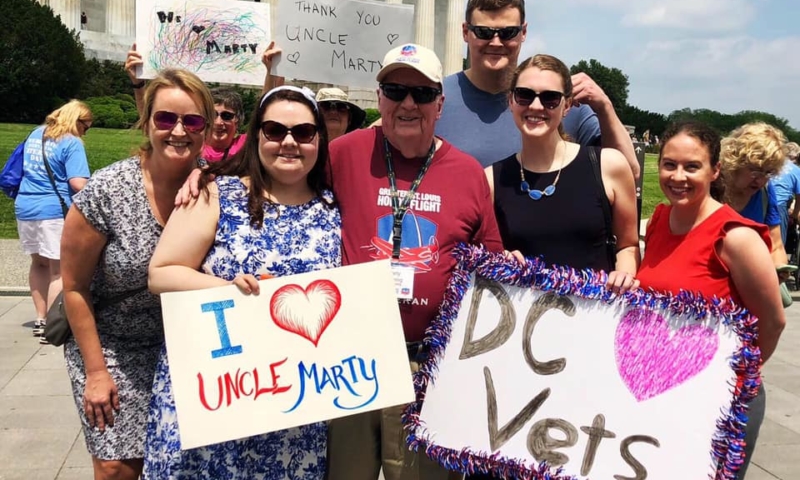 Members holding signs of thanks and love around a veteran in front of the Lincoln Memorial
