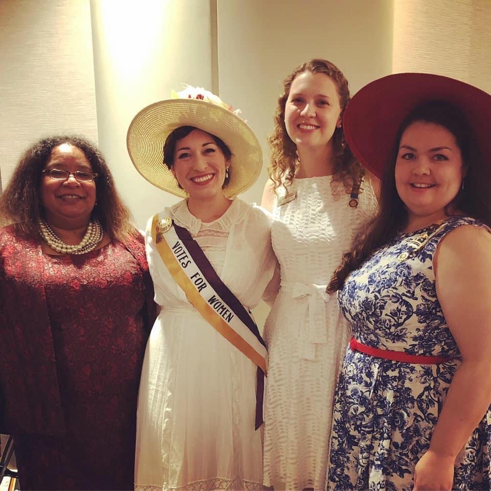 Four dress-up women, one wearing a suffragette costume